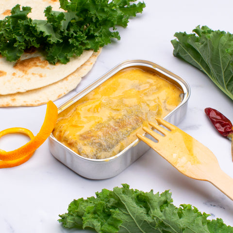 conserve de filets de truite en sauce curry ouverte sur une table blanche entouré de feuilles de salade