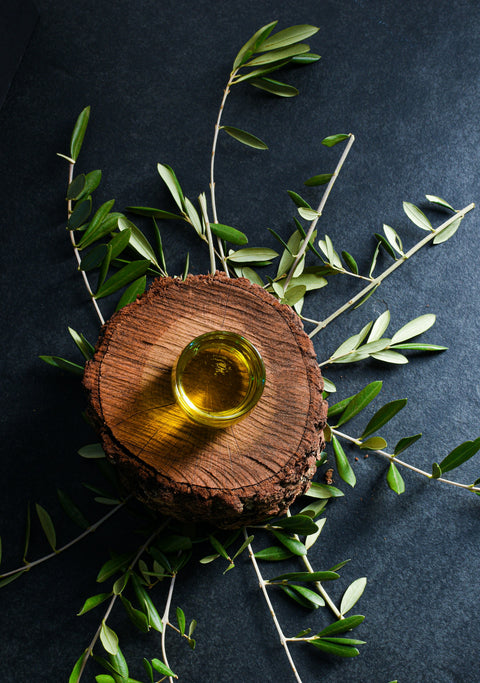 Huile d'olive dans un verre sur une pièce ronde en bois entouré de feuilles d'olivier